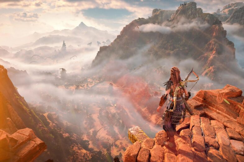 Aloy overlooking the Forbidden West from atop a tall cliff